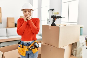 Canvas Print - Middle age grey-haired woman wearing hardhat standing at new home shocked covering mouth with hands for mistake. secret concept.