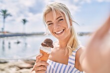 Young Blonde Girl Eating Ice Cream Making Selfie By The Camera At The Beach.
