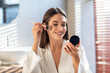 © Prostock-studio - Daily Makeup. Smiling Young Female Applying Blush With Makeup Brush In Bathroom