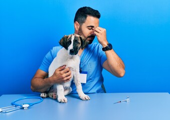 Poster - Handsome hispanic veterinary man with beard checking dog health tired rubbing nose and eyes feeling fatigue and headache. stress and frustration concept.