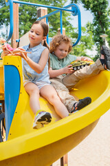 Wall Mural - full length view of brother and sister sitting on slide and playing with toys.