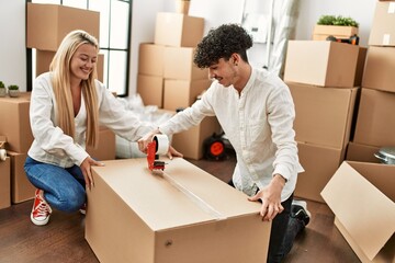 Poster - Young beautiful couple smiling happy packing cardboard box at new home.