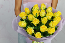 A Bouquet Of Yellow Roses With Open Buds And Green Leaves In A Delicate Purple Package In The Hands Of A Girl Without A Face On A Light Background