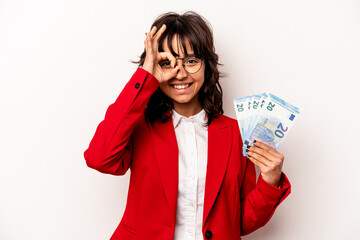 Wall Mural - Young business hispanic woman holding banknotes isolated on white background excited keeping ok gesture on eye.