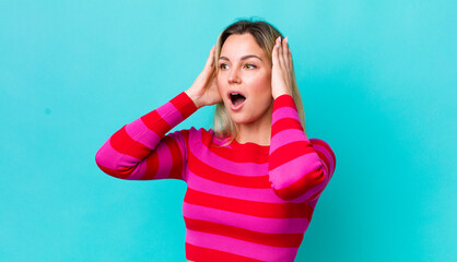 Wall Mural - pretty blonde woman feeling happy, excited and surprised, looking to the side with both hands on face