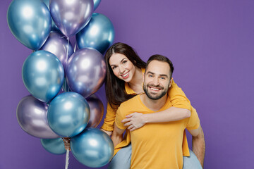 Wall Mural - Young couple two friends family man woman together in yellow clothes celebrating holiday party hold bunch air balloons give piggyback ride to joyful, sit on back isolated on plain violet background.