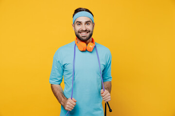 Wall Mural - Young fun fitness trainer instructor sporty man sportsman in headband blue t-shirt spend weekend in home gym hold skipping rope isolated on plain yellow background. Workout sport motivation concept.