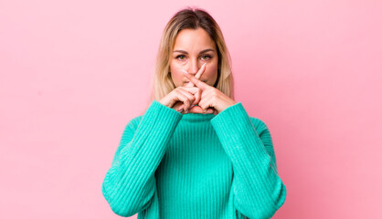 Wall Mural - pretty blonde woman looking serious and displeased with both fingers crossed up front in rejection, asking for silence