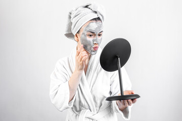 Poster - Young woman with a clay mask on her face in front of a mirror.