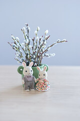 Sticker - Spring bouquet of willow branches in vase and cute little bunny toys on table, abstract gentle blurred background. Festive spring season