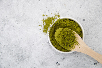 A bowl and a spoon with Matcha green tea powder on a gray table