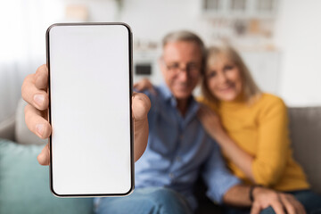 Happy senior couple showing cellphone with white empty screen, advertising application or website, mockup