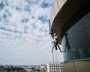 Wall Mural - Industrial mountaineering worker cleaning glass window of skyscraper. Male cleaner using safety lifting equipment while washing window of high-rise building.