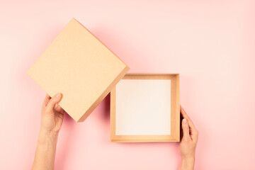 Wall Mural - Female hands open empty brown cardboard box on light pink background. Mockup parcel box. Top view, copy space. Packaging, shopping, delivery concept