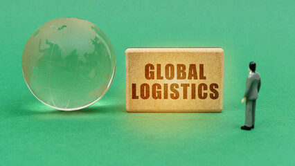 Wall Mural - On the green surface is a globe and a figurine of a man who looks at a sign with the inscription - Global Logistics