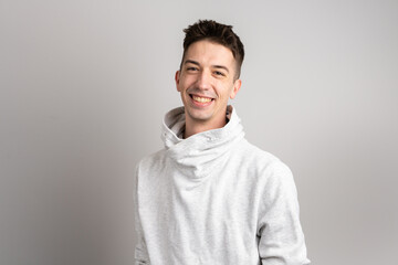 Wall Mural - Portrait of one adult caucasian man 25 years old looking to the camera in front of white wall background smiling wearing casual white hoodie copy space