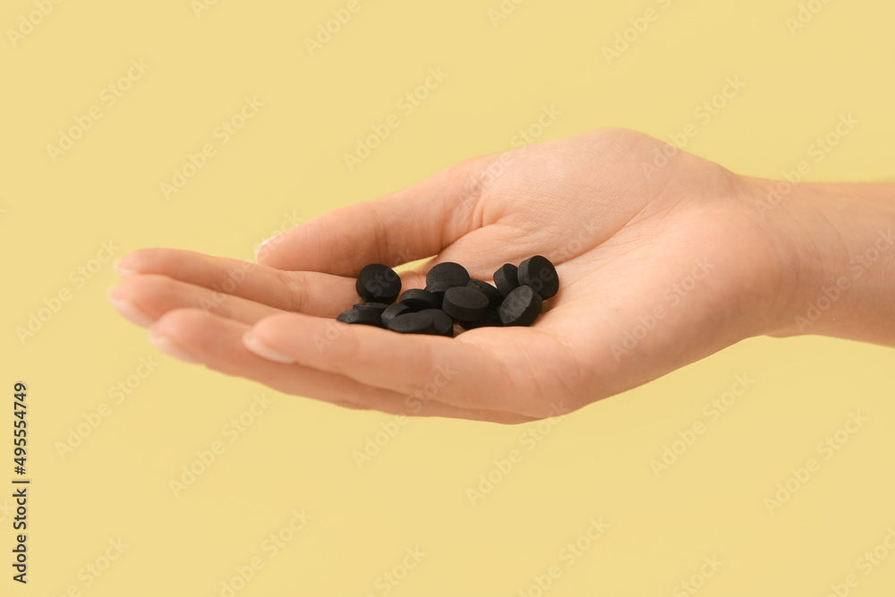 Female hand with activated carbon pills on color background, closeup