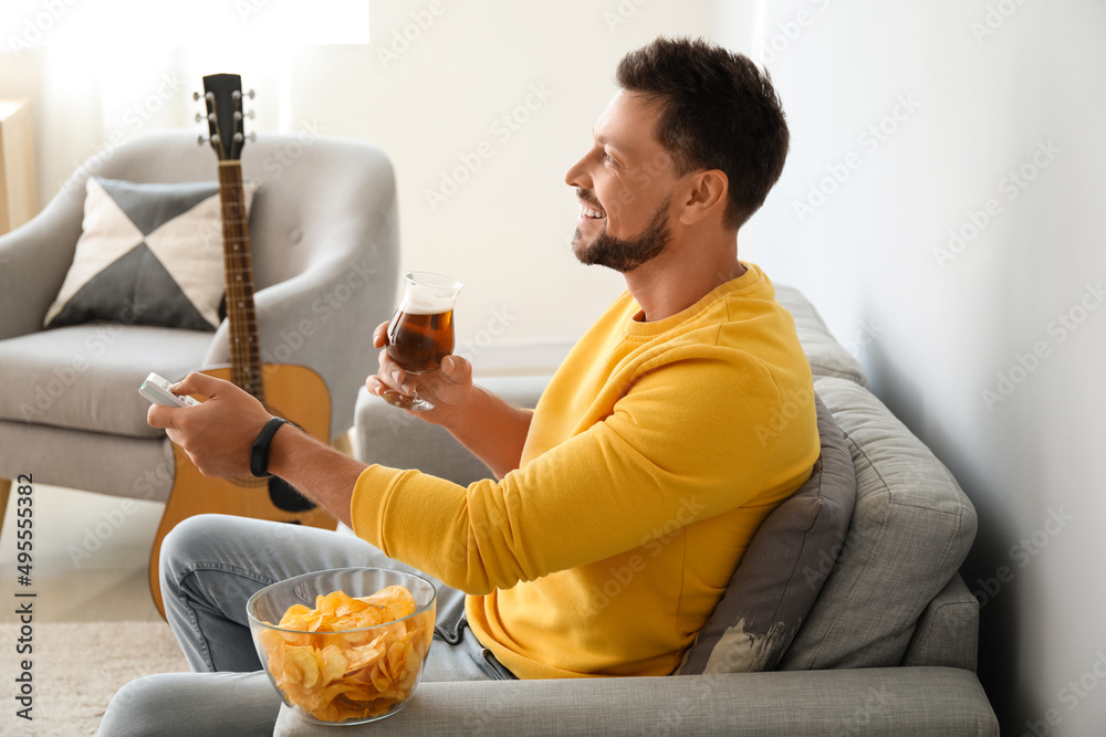Handsome man drinking beer while watching TV at home