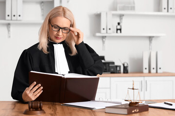 Poster - Mature female judge reading book at table in courtroom