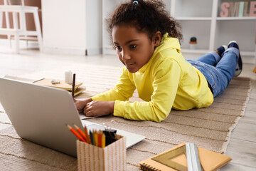 Canvas Print - Little African-American girl writing in copybook while studying with online tutor on floor at home