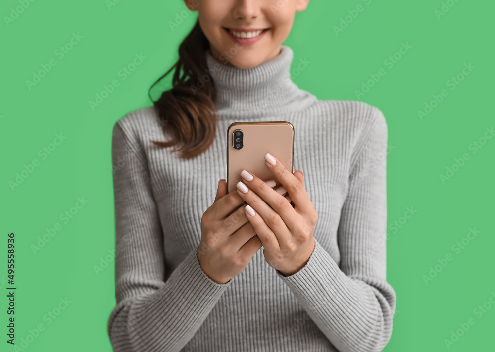 Beautiful young woman with mobile phone on green background