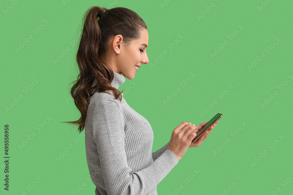 Beautiful young woman with mobile phone on green background