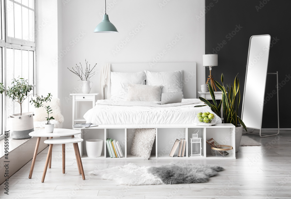 Stylish interior of light bedroom with comfortable bed and modern laptop