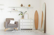 Interior of light living room with wooden surfboard, armchair and commode