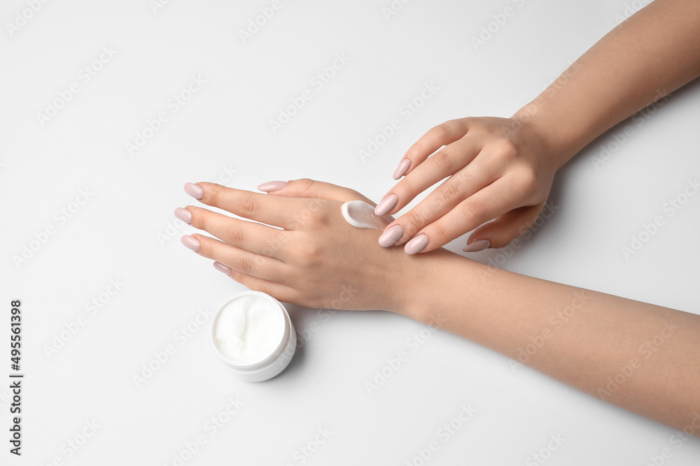 Woman with beautiful manicure applying cream on white background, closeup