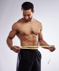 Poster - Almost at my ideal weight. Shot of a man measuring his waist using a measuring tape against a studio background.