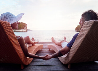 Poster - Just the two of us. Rearview shot of a cheerful young couple holding hands while relaxing on deck chairs and looking out at the ocean outside during the day.