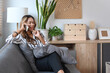© Prathankarnpap - Beautiful millennial woman resting on couch at home and talking on mobile phone.