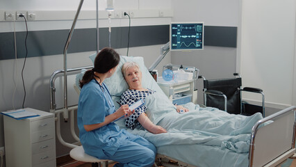 Wall Mural - Nurse giving assistance to senior patient with disease in bed. Medical assistant and doctor doing healthcare checkup for pensioner with oxygen tube and IV drip bag in hospital ward.