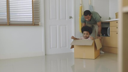 Wall Mural - Happy playful African American father and son having fun sitting in cardboard on moving day. Black African man playing with his little boy riding in box.