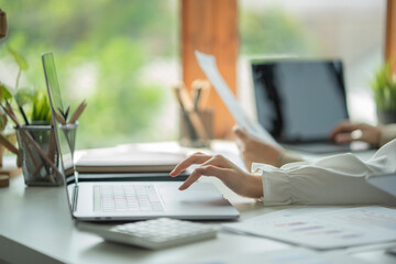 Fototapete - Woman sitting at desk and connecting with her laptop, she is working and typing on the keyboard, hands close up