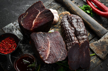 Wall Mural - Dried veal beef with spices and herbs. On a black stone background. Top view. Free space for text.