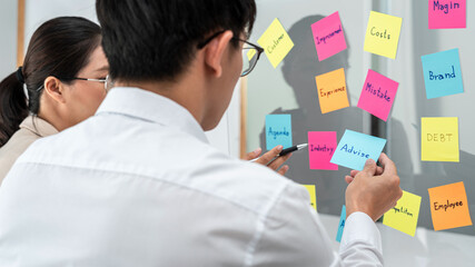 Poster - Two business people holding keyword in notes on a glass wall to brainstorm about new business project for planning marketing plan together in office