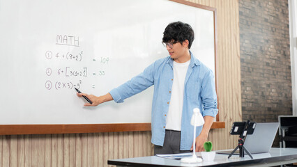 Male tutor standing in front of whiteboard and writing math equations on board to explaining new lesson