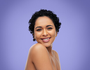 Wall Mural - beauty and people concept - portrait of happy smiling young african american woman with bare shoulders over violet background