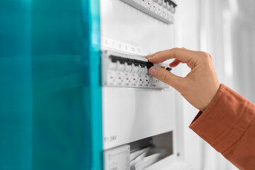 electricity, energy and power consumption concept - close up of hand switching electric board at home