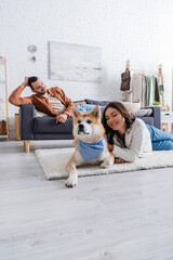 Wall Mural - happy young woman hugging akita inu dog near boyfriend on couch.