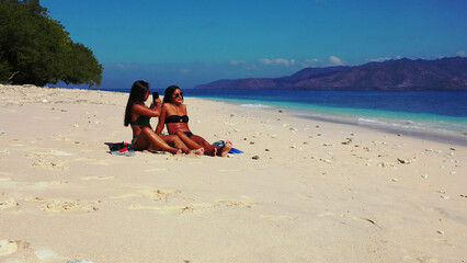 Poster - Girls calmly relax on a beach with fine white sand bordered by a turquoise sea.Gili Meno, Indonesia