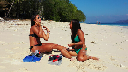 Poster - Girls calmly relax on a beach with fine white sand bordered by a turquoise sea.Gili Meno, Indonesia