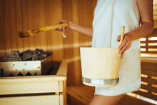 Woman In Sauna - Real, Authentic Moment. Women Pouring Water To Hot Stones To Produce Steam. Attractive And Smiling Woman In Towels Holding Wooden Washtub In Sauna