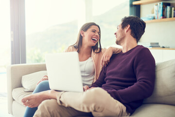 Canvas Print - Sharing an online laugh. Shot of a smiling young couple using a laptop while relaxing on the sofa at home.