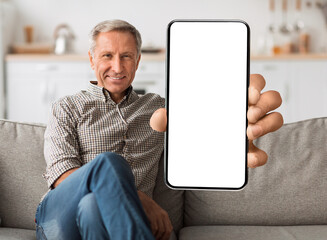 Poster - Cool mobile application. Smiling senior man showing cellphone with white blank screen, sitting on sofa at home, mockup