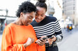 © ADDICTIVE STOCK - Cheerful black women browsing smartphones on street