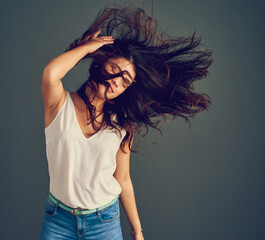 Wall Mural - Her hair has a mind of its own. Studio shot of a carefree young woman holding her hair while it gets blown by wind as she stands against a dark background.