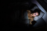 Fototapeta Zwierzęta - Pretty, middle-aged woman using her cell phone in bed at night - unhealthy  blue light exposure