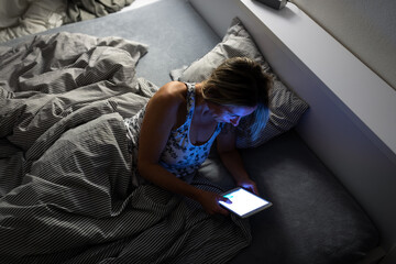 Pretty, middle-aged woman using her tablet computer before sleep in bed in the evening